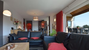 A modern living room with a black leather sofa, a wooden coffee table, and a dining area in the background. - Robertville Lakeview Escape (Waimes)