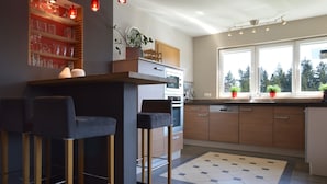 A modern kitchen with a bar area, wooden cabinets, and a large window with a view of trees. - Robertville Lakeview Escape (Waimes)