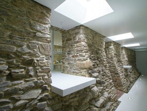 Interior de pared de piedra con un estante blanco, tragaluces y una zona de baño visible.