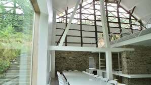 A modern interior with a long dining table, white chairs, and a stone wall. - Grand Retreat in Redu (Libin)