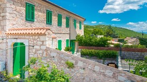 A stone building with green shutters, a tiled roof, and a view of a hillside. - Apartment Crikvenica Near Sandy Beach (Crikvenica)