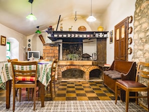 Traditional kitchen with a brick oven, dining table, and bookshelf, offering a homely atmosphere.