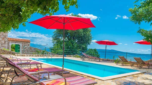 A pool area with lounge chairs and red umbrellas, stone flooring, and a view of the sea. - Apartment Crikvenica Near Sandy Beach (Crikvenica)
