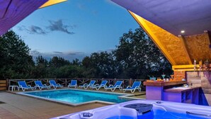 Un área de piscina con dos jacuzzis, sillas de descanso y una zona de bar.