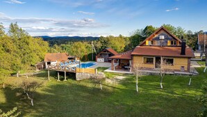 Una casa de dos pisos con piscina, un deck con sillones de descanso y vistas a las montañas.