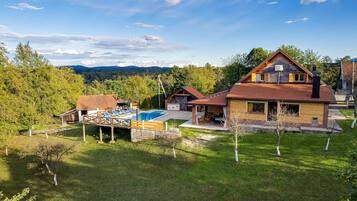 Una casa de dos pisos con piscina, un deck con sillones de descanso y vistas a las montañas.