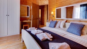 Un dormitorio de cabaña de madera con cama, mesitas de noche, un espejo y un armario.