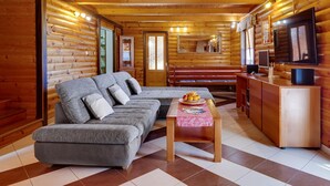Interior de una cabaña de troncos con un sofá, una mesita con fruta, un televisor y un armario de madera.