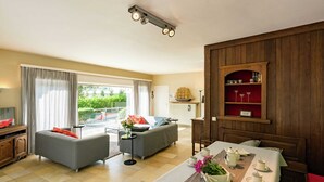 A modern living room with a sofa, a dining table set with cups and a vase of flowers, and a wooden cabinet with shelves. - Oostduinkerke Forestside Villa (Koksijde)