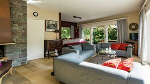 A living room with a stone fireplace, a sofa set, a coffee table, and a dining area with a table and chairs. - Oostduinkerke Forestside Villa (Koksijde)