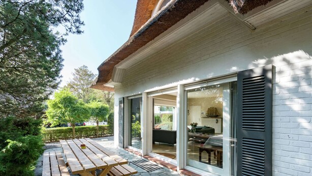 A patio area with a wooden table and benches, a stone pathway, and a white building with black shutters. - Oostduinkerke Forestside Villa (Koksijde)