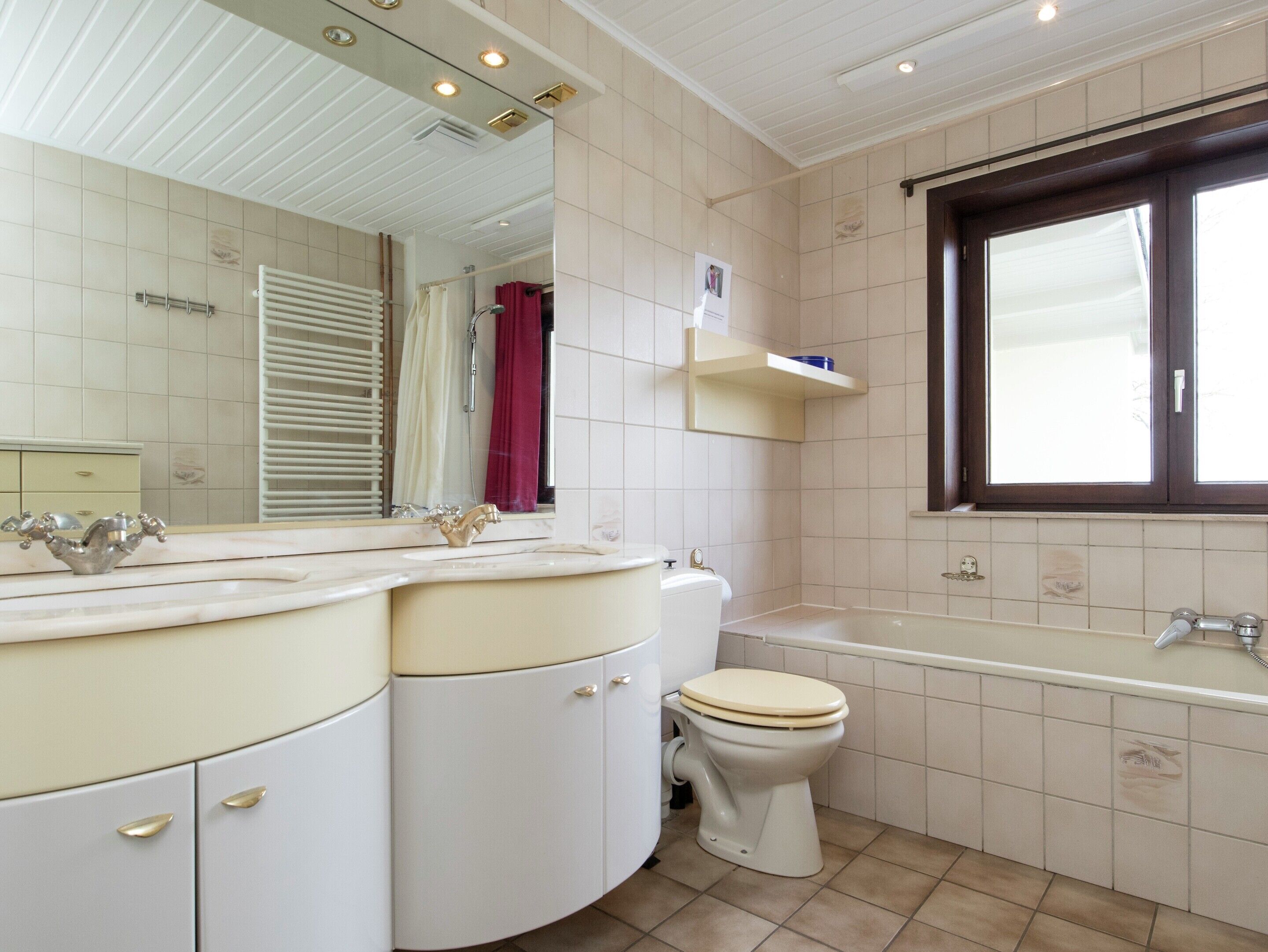 A bathroom with a white vanity, a toilet, a bathtub, and a window.