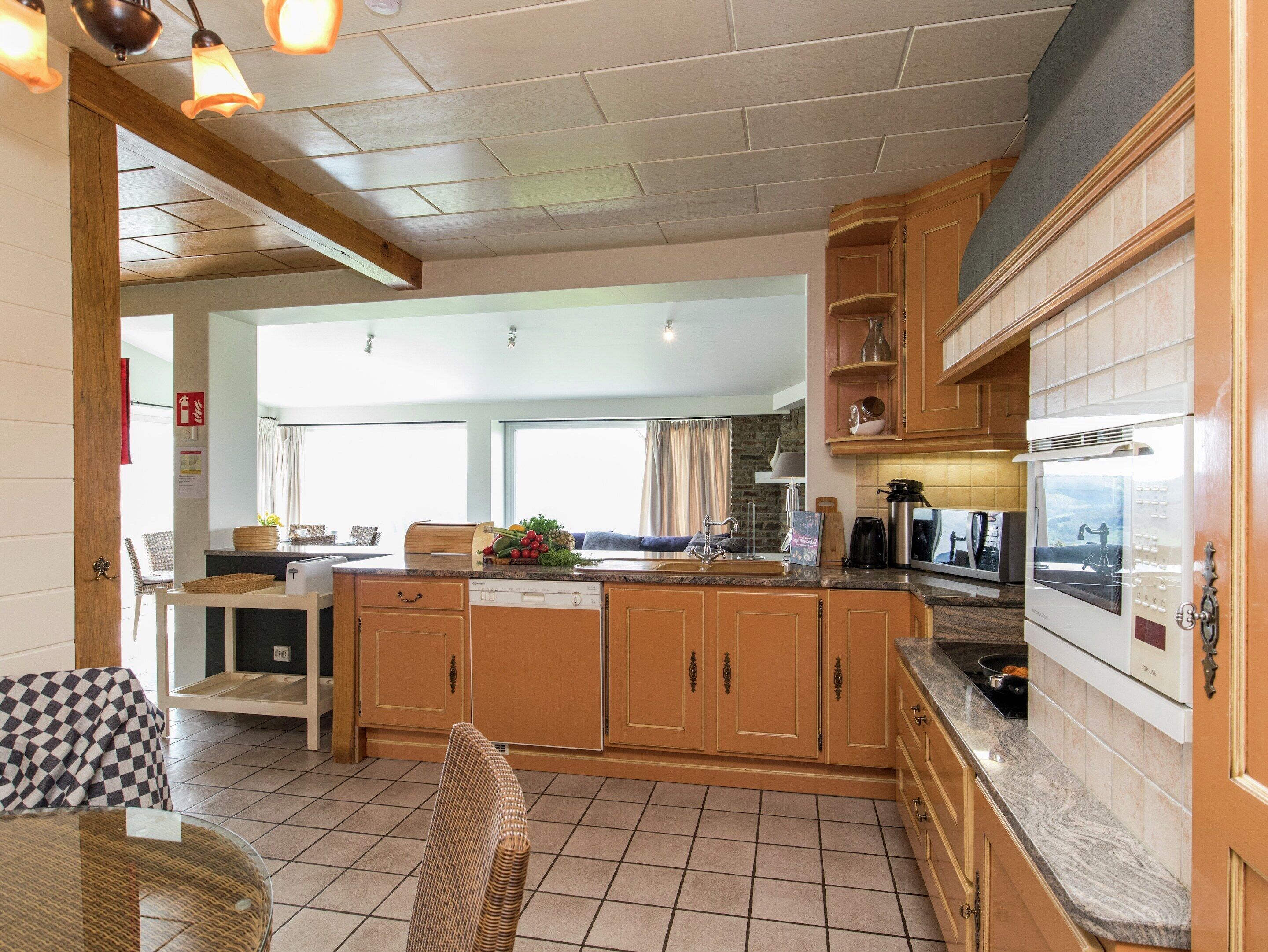 A kitchen with wooden cabinets, a built-in oven, and a dining area with a wicker chair.
