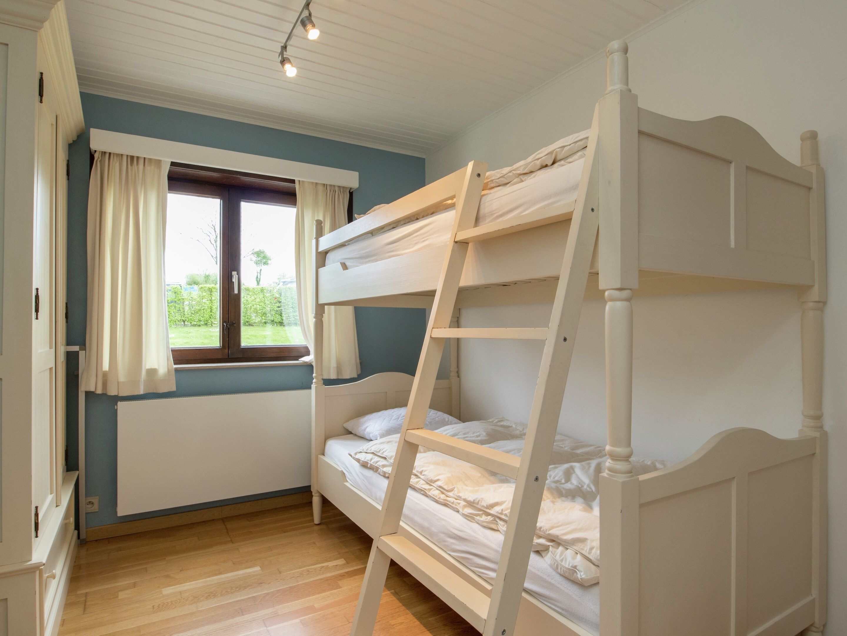 A bunk bed room with a window, wooden floor, and a radiator.