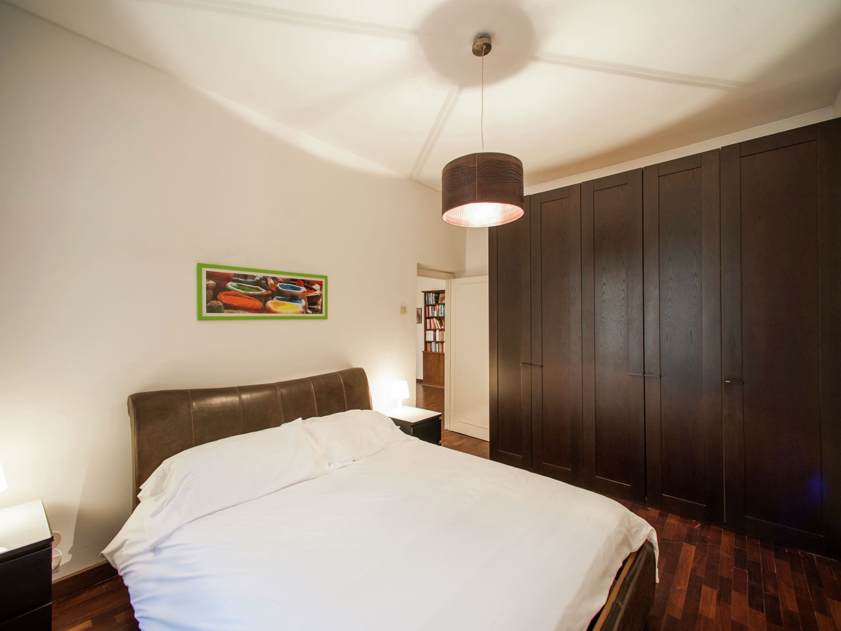 Un dormitorio con una cama grande, un armario de madera, una mesita de noche y una lámpara fijada en la pared.