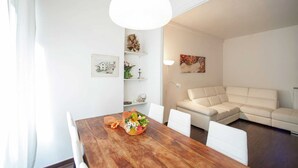 Un soggiorno moderno con un tavolo da pranzo in legno, sedie bianche, un divano beige e un'ampia finestra con tende leggere.