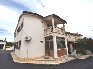 A two-story house with a balcony, a visible air conditioning unit, and a stone foundation. - Comfortable Holiday Home Only 500m to the sea With Outdoor Kitchen, Wifi and Airco (Medulin)