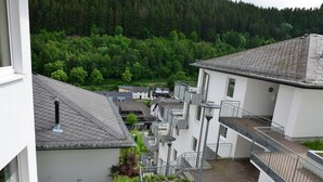 Un edificio de varios pisos con terraza en la azotea, área de recepción y vistas a una ladera boscosa.