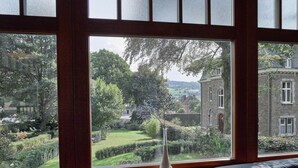 A room with a large window offering a view of a garden and a stone building. - Stavelot Sauna & Garden Stay (Stavelot)