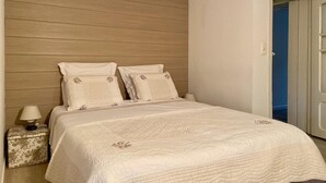 A bedroom with a wooden headboard, a bed with white bedding, a nightstand with a lamp, and a door leading to another room. - Stavelot Sauna & Garden Stay (Stavelot)