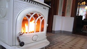 A white wood-burning stove with a glass door, a metal handle, and a decorative base. - Stavelot Sauna & Garden Stay (Stavelot)