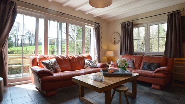 Ein gemütliches Wohnzimmer mit Ledersofa, einem Holztisch und großen Fenstern mit Blick ins Freie.