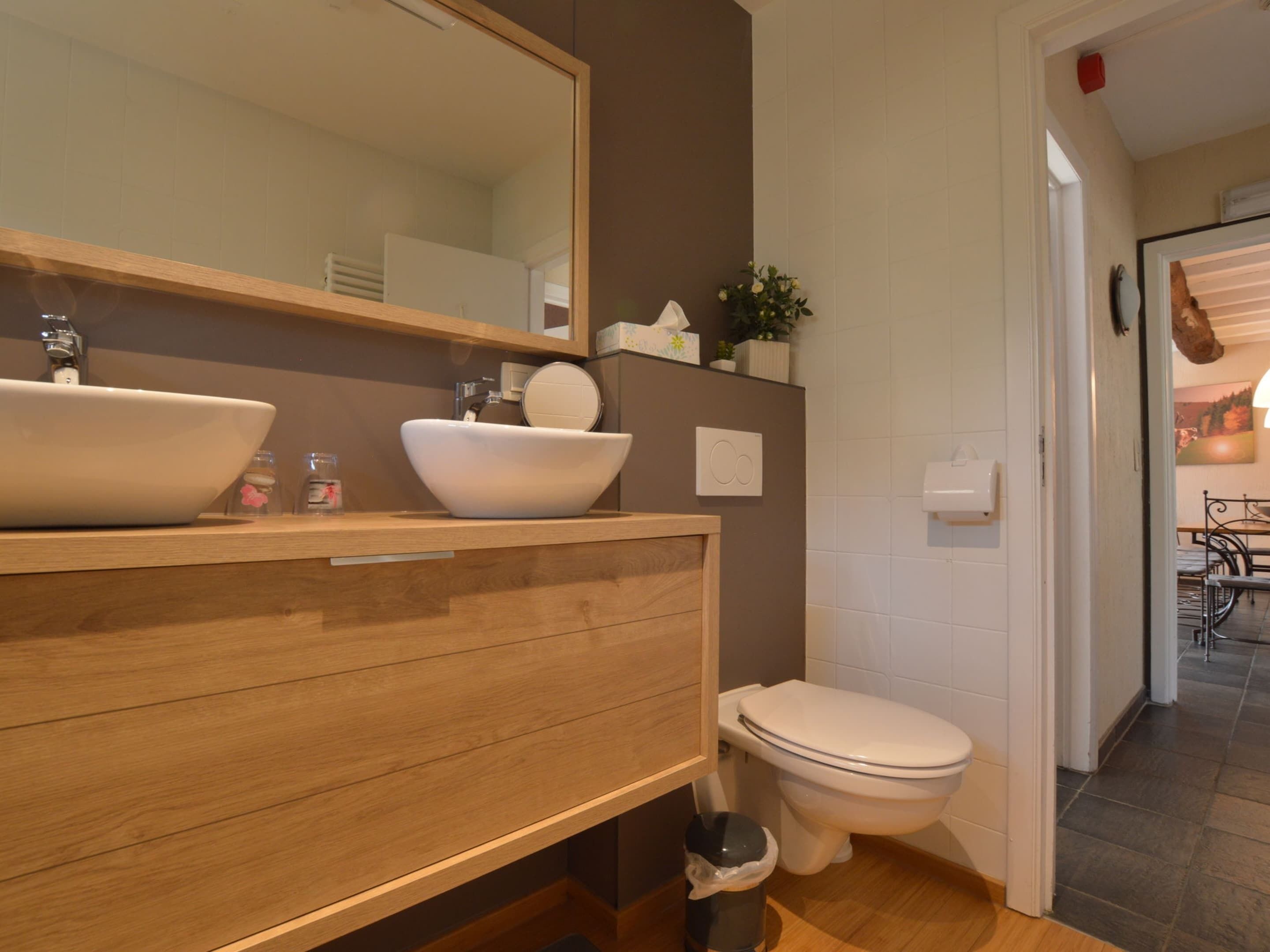 A modern bathroom with two vessel sinks, a mirror, a toilet, and a trash bin.