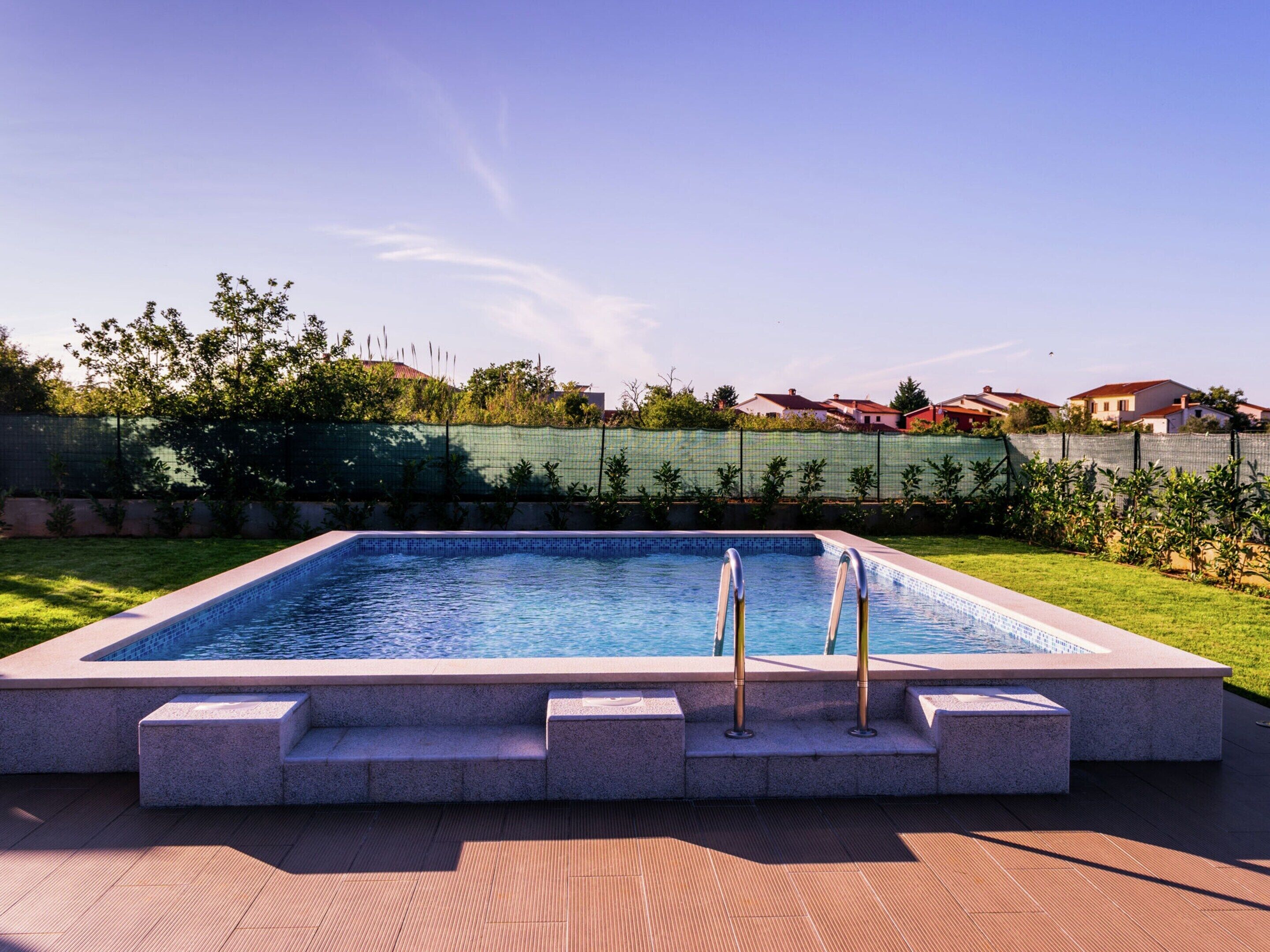 A rectangular swimming pool with steps leading into it, surrounded by a paved deck.