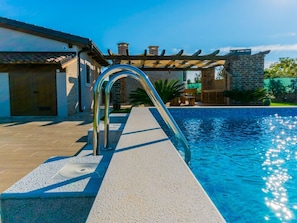 A swimming pool with a metal ladder, a pergola, and a stone building in the background. - Lovely Holiday Home in Fazana With Swimming Pool (Fazana)