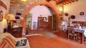 A rustic interior with a stone wall, wooden beams, a dining area with a table and chairs, and a cozy sitting area with a sofa.