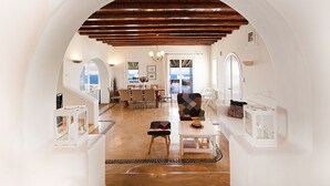 Interior espaçoso com teto alto, vigas de madeira, área de jantar central e vista através de uma porta em arco.