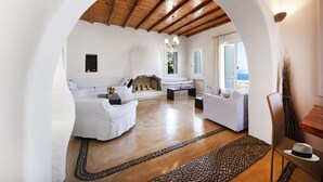 Uma sala de estar ampla com lareira, mobiliário branco e vista através de um arco.