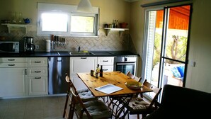 A kitchen with white cabinets, a wooden dining table, and a large window. - Holiday Home With Garden in Kritinia (Rhodes)