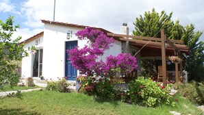 A white building with a blue door, surrounded by a garden with purple flowers and a wooden pergola. - Holiday Home With Garden in Kritinia (Rhodes)