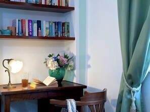 Un'area studio con una scrivania in legno, scaffali, un vaso con fiori, una lampada e una sedia.