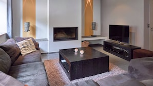 A modern living room with a sofa, a coffee table, a TV, and a fireplace. - Spa Apartment With Private Pool (Spa)