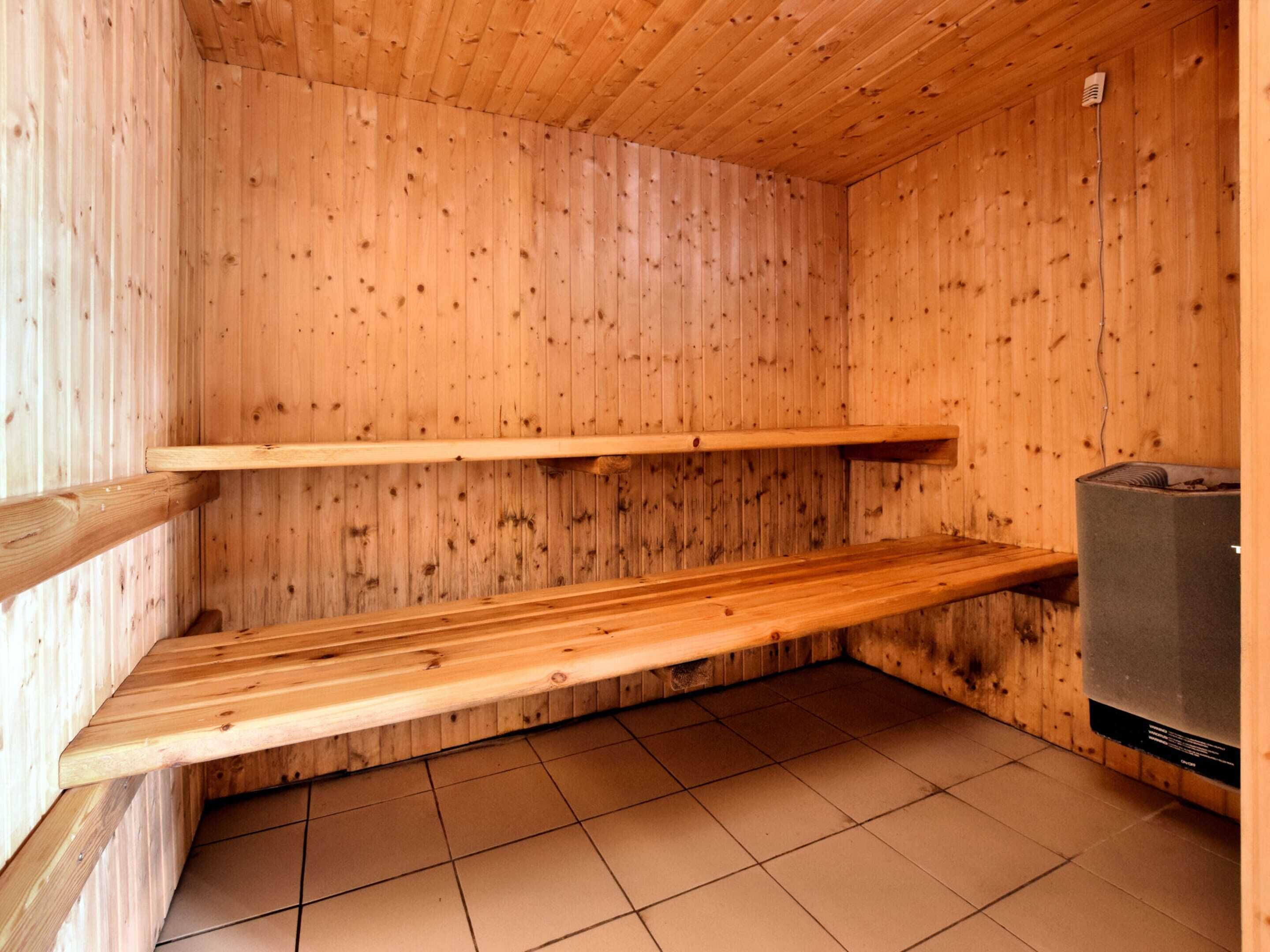 Un cuarto de sauna con paredes de madera y piso de baldosas, que incluye dos bancos y un equipo de sauna.
