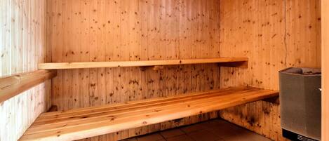 Un cuarto de sauna con paredes de madera y piso de baldosas, que incluye dos bancos y un equipo de sauna.