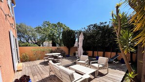 Una terraza de madera con mobiliario exterior, una maceta azul y un árbol.