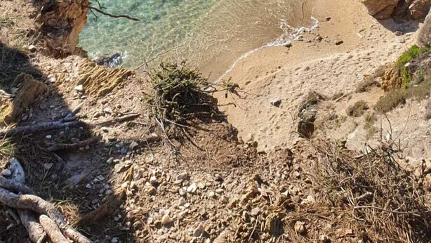 Paisaje costero rocoso con aguas poco profundas y transparentes, una playa de arena y vegetación escasa.