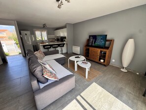 Una sala de estar moderna con un sofá, dos mesitas, un televisor y un mueble de almacenamiento.