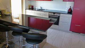 A modern kitchen with red cabinets, a black countertop, and a stainless steel oven. There are three bar stools in front of the counter. - Chalet in Heremence With Stunning Alpine Views (Heremence)