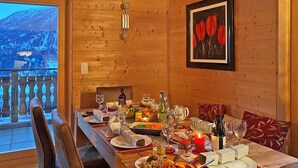 A wooden dining table set with plates, glasses, and candles, with a scenic view through a window. - Chalet in Heremence With Stunning Alpine Views (Heremence)