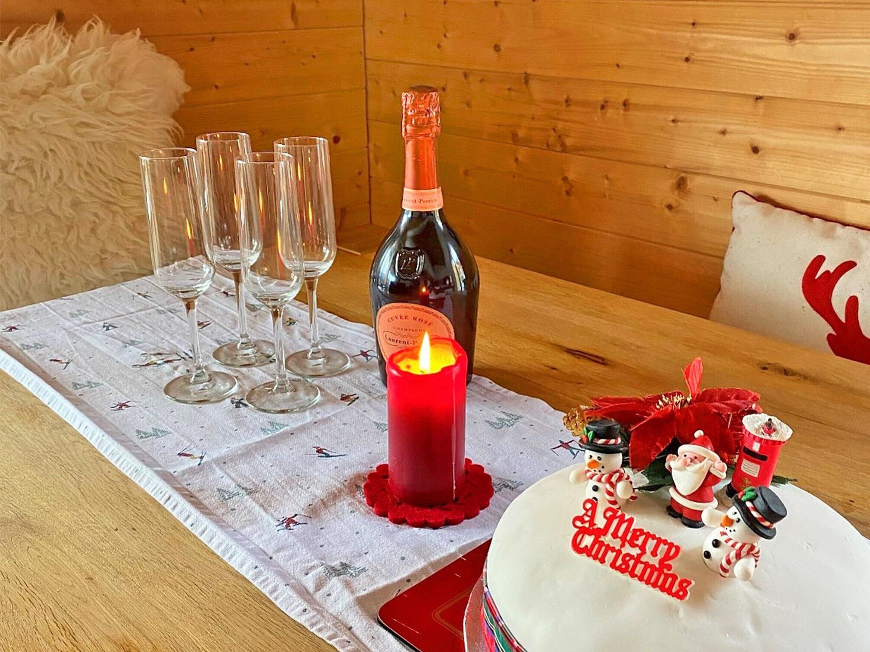 A table with a bottle of champagne, glasses, a lit candle, and a Christmas cake with decorations.