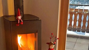 A wood-burning stove with a decorative gnome on top, a plush reindeer figure next to it, and a view of a snowy landscape through a glass door. - Chalet in Heremence With Stunning Alpine Views (Heremence)