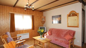 A cozy room with wooden walls, a pink sofa, wooden chairs, a wooden table, a ceiling fan, a TV, and a mirror. - Holiday Home in Nysted by Baltic Sea (Saas-Balen)