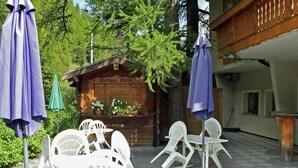 An outdoor seating area with white plastic chairs and tables, surrounded by potted plants and a wooden sign with flowers. - Holiday Home in Nysted by Baltic Sea (Saas-Balen)