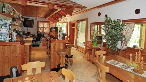 A wooden interior with a bar area, dining tables, chairs, and a large potted plant. - Holiday Home in Nysted by Baltic Sea (Saas-Balen)