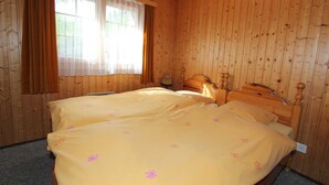 A room with wooden paneling, two beds with floral bedding, a window with curtains, and a nightstand with a lamp. - Holiday Home in Nysted by Baltic Sea (Saas-Balen)