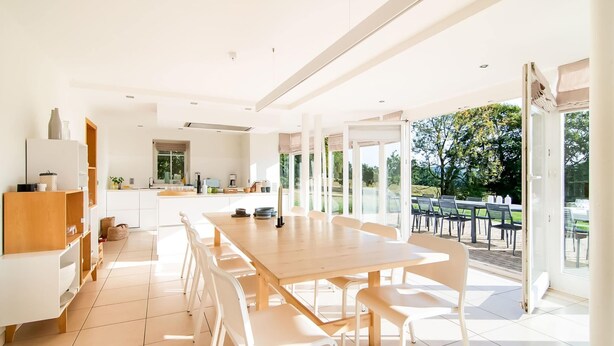 A modern kitchen with a large dining area, white cabinetry, and a view of the outdoors. - Luxurious Villa With Pool and Sauna, and Very Suitable for Culinary Workshops (Waimes)